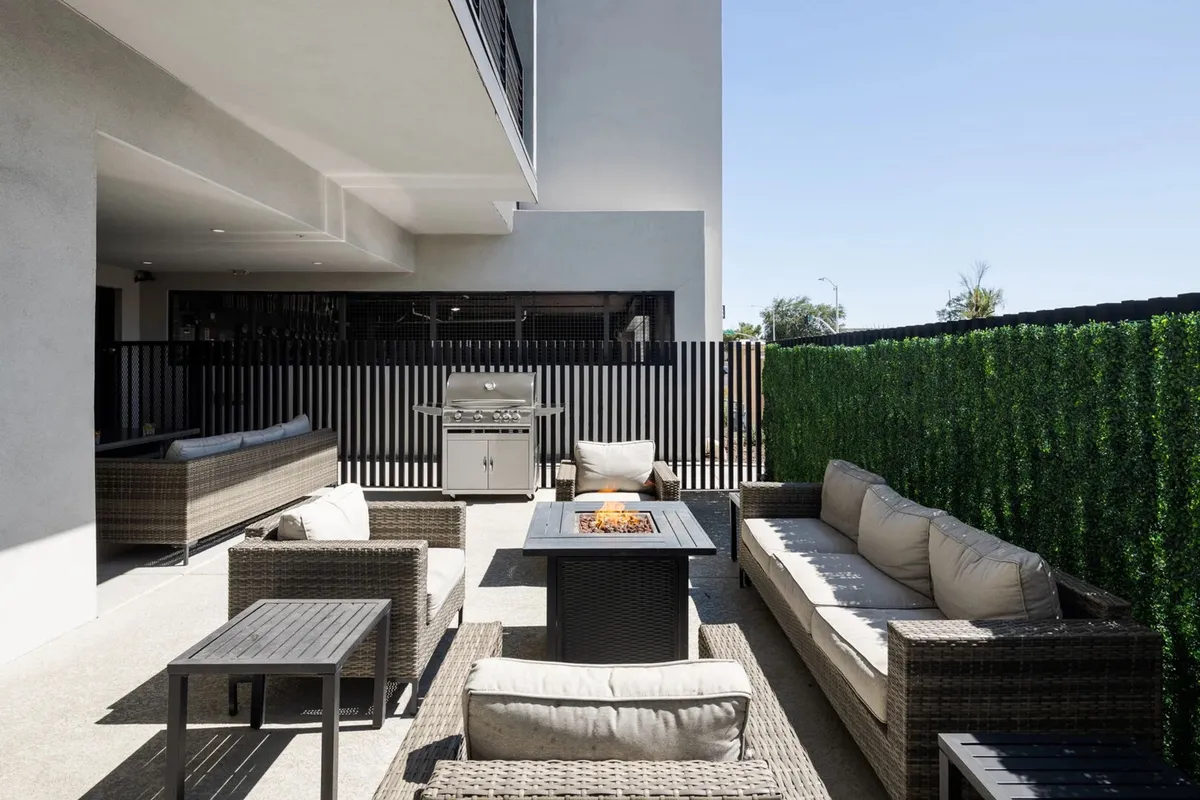 An outdoor communal area featuring a cozy fire pit, a grill for barbecuing, and ample seating surrounded by greenery. The scene is set for sunset dinners, weekend cookouts, or gathering with friends around the fire.