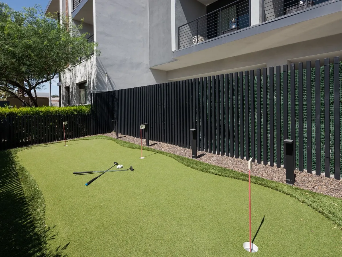 A well-manicured putting green with golf clubs resting on the grass, enclosed by a fence for privacy and safety. The setting is bright, recreational, and ideal for friendly competition or practicing your short game in the sun.
