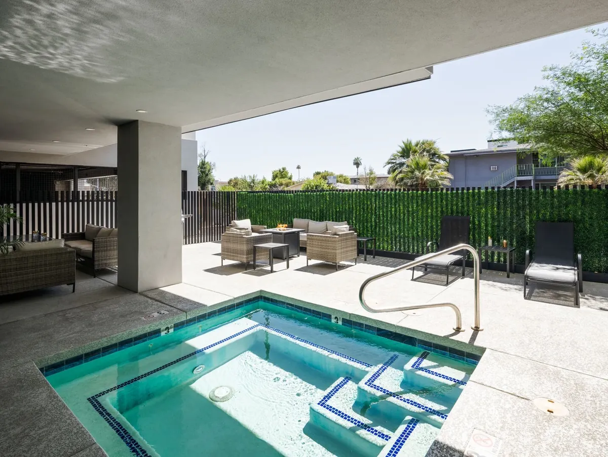 An inviting exterior shot of a relaxing hot tub surrounded by comfortable outdoor seating, lush landscaping, and a secure fenced yard. The warm lighting suggests a perfect spot for an evening soak or socializing under the stars.
