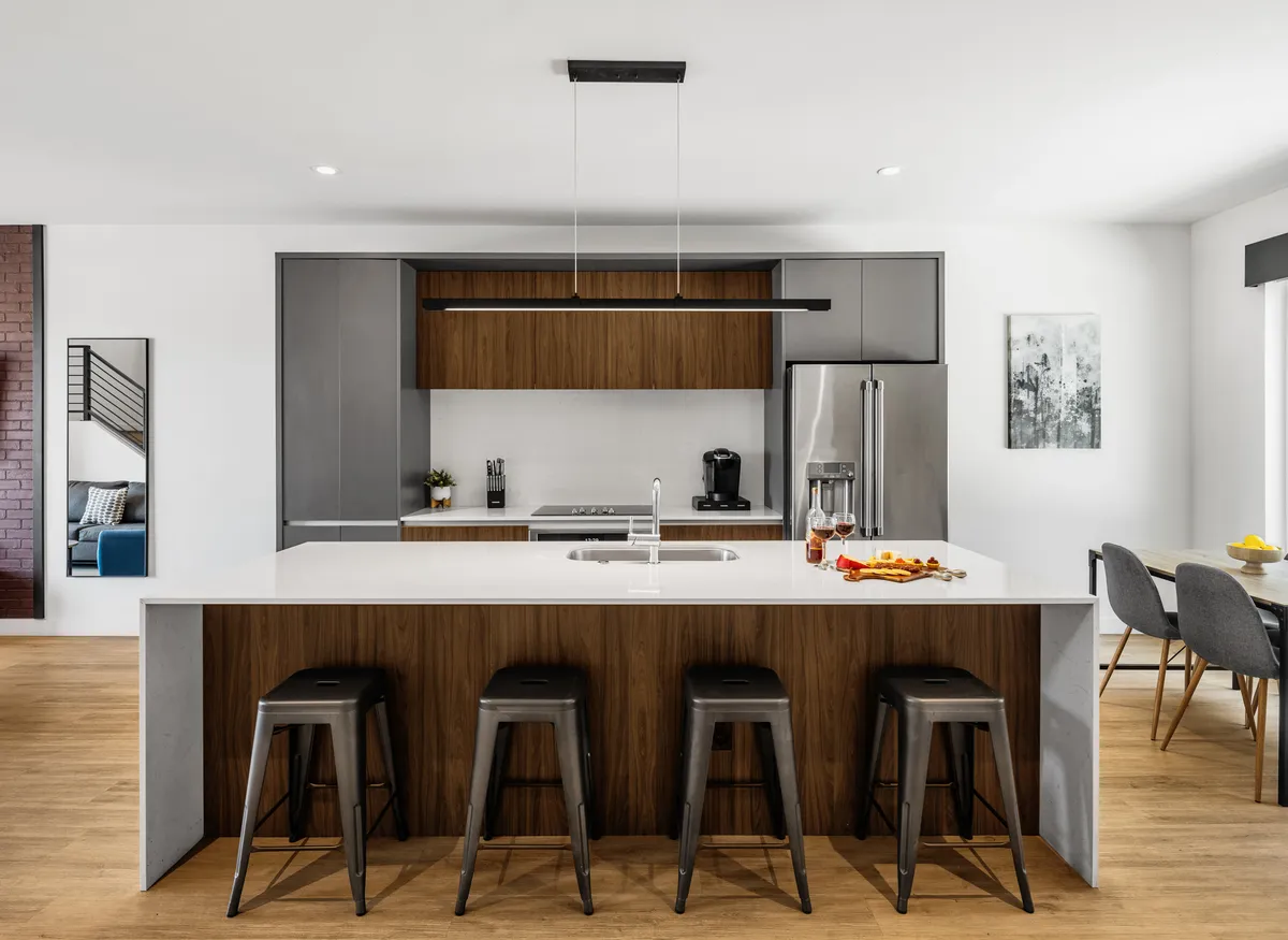 This image features a welcoming, modern kitchen with a central island surrounded by stools, high-end appliances, and an adjacent dining area. The space is bright and open, inviting for gatherings and meal preparation.