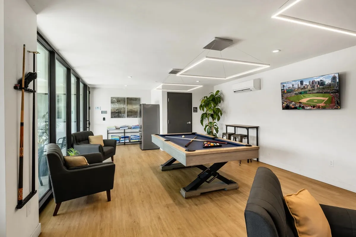 An inviting interior scene of a stylish clubhouse featuring a pool table, comfortable seating area, and a television, with touches of greenery for ambience. The setup encourages friendly games and socializing after a night out.